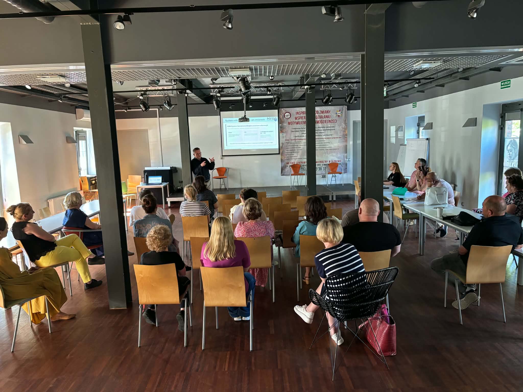 Szkolenie z&nbsp;zakresu RODO prowadzone w&nbsp;sali konferencyjnej. Uczestnicy siedzą na&nbsp;krzesłach ustawionych naprzeciw prelegenta oraz&nbsp;ekranu z&nbsp;prezentacją. Spotkanie ma profesjonalny i&nbsp;spokojny charakter, a&nbsp;jego celem jest poszerzanie wiedzy i&nbsp;podnoszenie standard&oacute;w bezpieczeństwa danych oraz&nbsp;jakości obsługi klient&oacute;w.