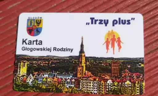 „Karta Głogowskiej Rodziny ‘Trzy plus’” — kolorowa karta rabatowa z Głogowa (Polska), skierowana do rodzin wielodzietnych. Na karcie widoczne są: herb Głogowa, hasło „Trzy plus”, grafika przedstawiająca rodzinę (rodzice z dzieckiem) oraz stylizowana panor