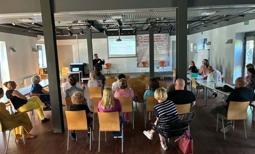 Szkolenie z zakresu RODO prowadzone w sali konferencyjnej. Uczestnicy siedzą na krzesłach ustawionych naprzeciw prelegenta oraz ekranu z prezentacją. Spotkanie ma profesjonalny i spokojny charakter, a jego celem jest poszerzanie wiedzy i podnoszenie stand